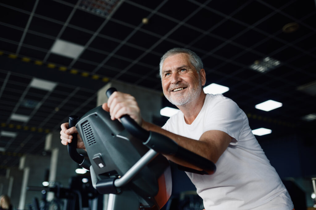 Elderly man poses on exercise bike in gym - Os Melhores Alimentos para Aumentar a Massa Muscular em Idosos e Garantir Força e Vitalidade!